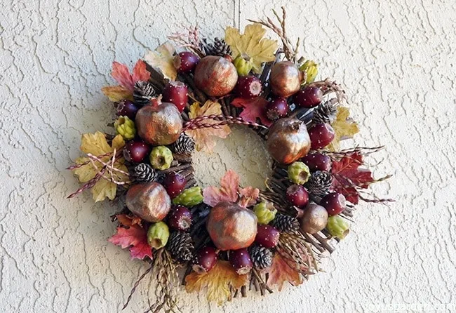 a homemade fall wreath desert style using a twig wreath, pomegranates, cones, pods & fall leaves