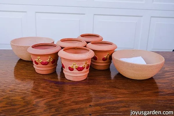 2 terra cotta bowls & 5 terra cotta pots painted  with red & gold sit on a table