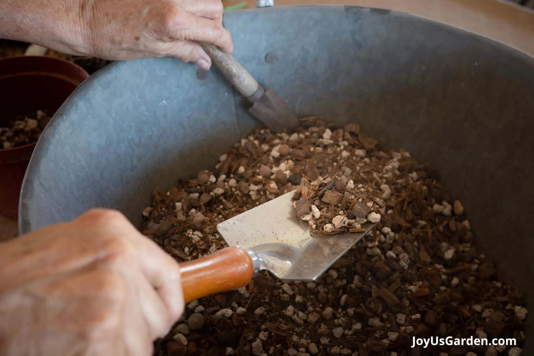 A silver metal bin holds succulent & cactus mix with a trowel & a mini trowel digging into the mix.