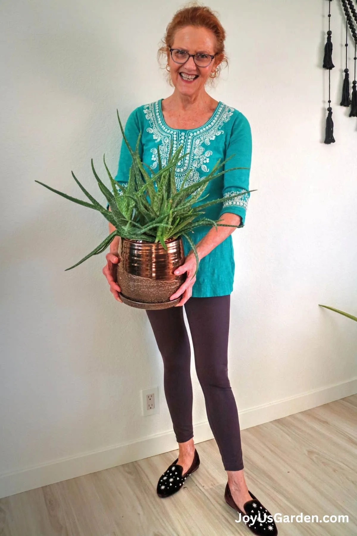 A woman holding an aloe vera plant in a bronze pot.